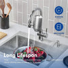 A stainless steel faucet water filter is installed on a kitchen sink, with a glass bowl filled with filtered water.