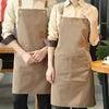 A woman wearing a tan canvas kitchen apron with large pockets and brown leather straps.