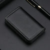 A black stitched PU leather card holder wallet resting on a dark surface next to a pen.