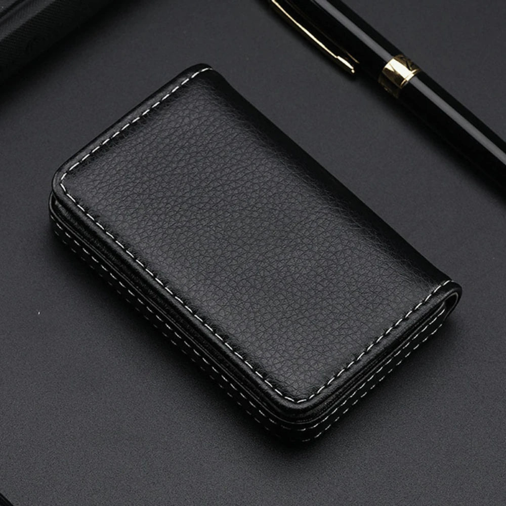 A black stitched PU leather card holder wallet resting on a dark surface next to a pen.