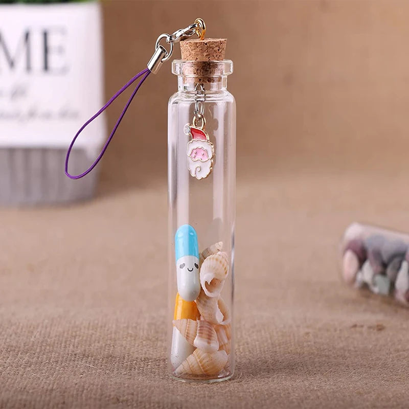 A glass bottle with a cork stopper, featuring a pink charm and small seashells inside.