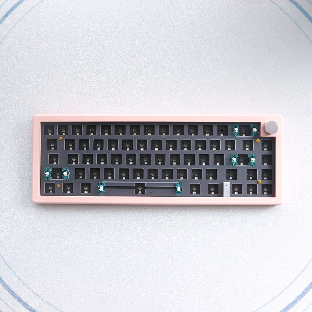 Teclado mecánico rosa de 67 teclas con cambio rápido, iluminación RGB y perilla de volumen sobre una superficie blanca.
