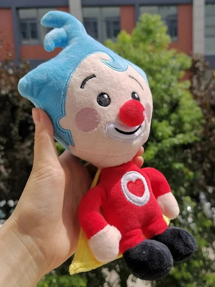 A hand holds a soft, blue-haired clown plush toy with a red nose and a red shirt against a blurred green background.