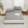 A gray waterproof mattress protector with elastic straps is displayed on a bed, next to a white nightstand and window.