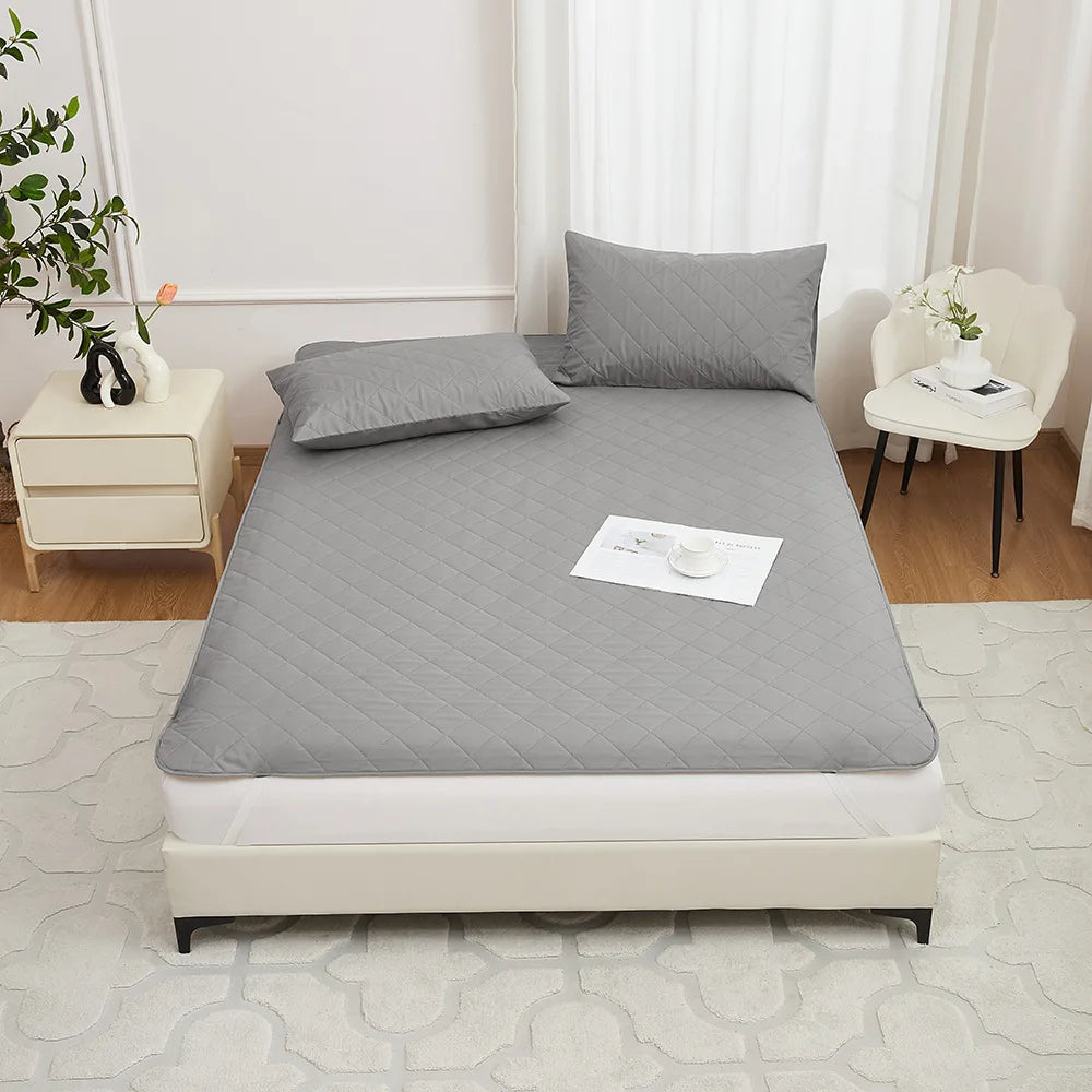 A gray waterproof mattress protector with elastic straps is displayed on a bed, next to a white nightstand and window.