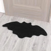 Black decorative rug shaped like a Halloween spider web with a ghost design placed on a light wood floor.
