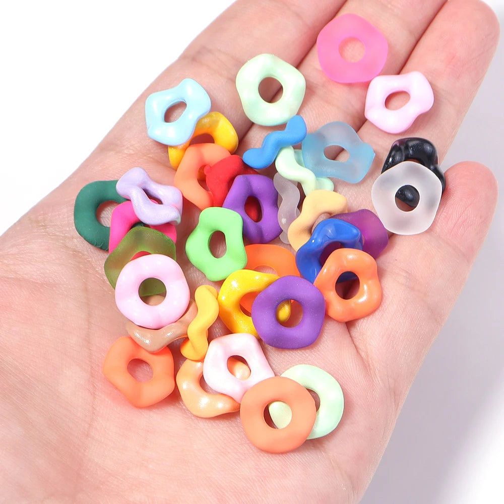 A hand holds a collection of colorful acrylic spacer beads with wave patterns for jewelry making