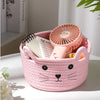 A pink woven cotton rope storage basket shaped like a cat face holds a small pink fan.