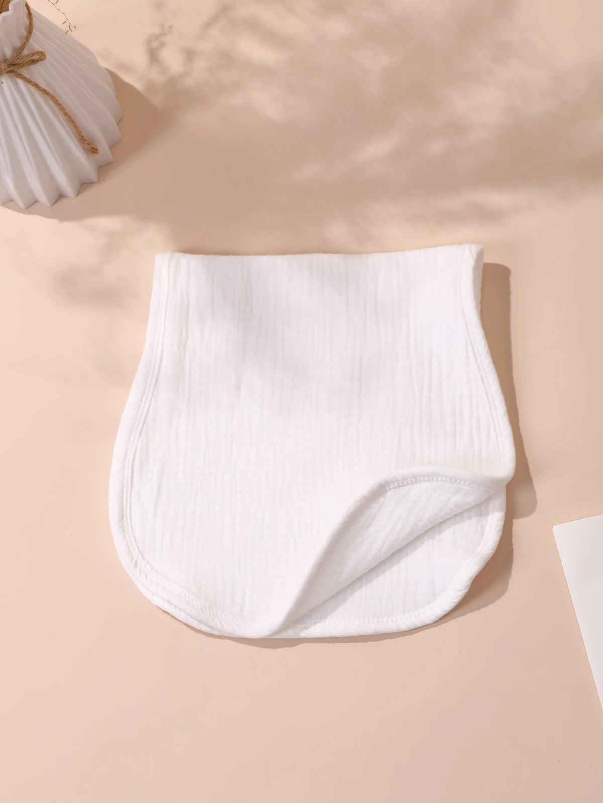 A white, ribbed baby burp cloth is displayed on a light pink surface.