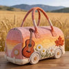 A pink quilted travel duffle bag with orange handles and 3D stitching resting on a wooden surface.