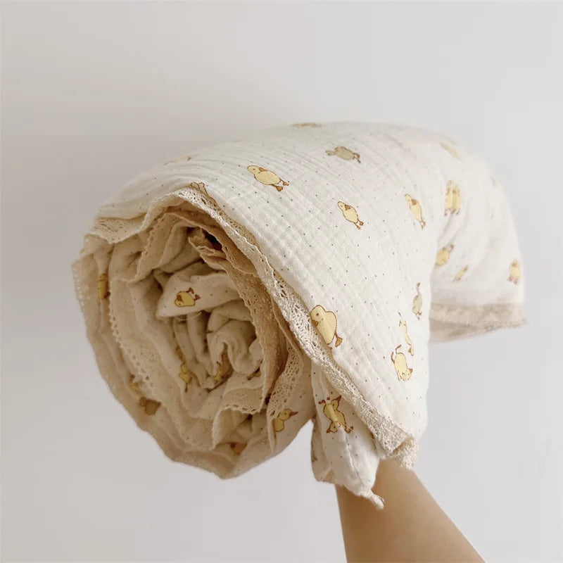 A rolled floral muslin baby blanket in off-white with small gold floral patterns.