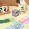 A collection of pink and green quilted fabric strips stacked on a table next to a mug and wooden frame.