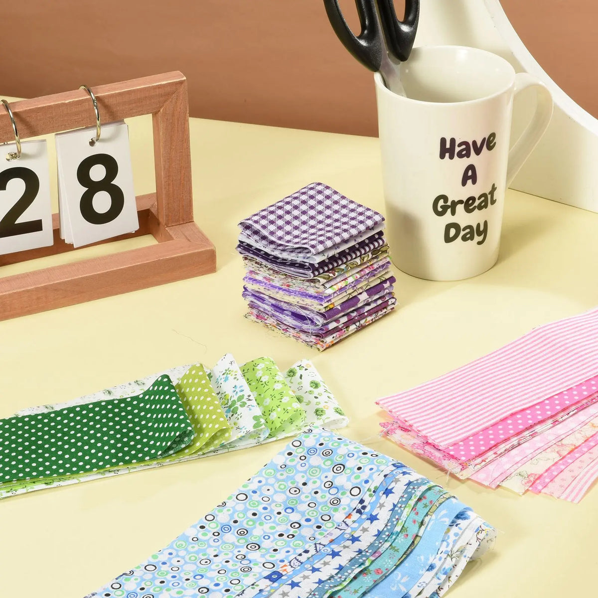 A collection of pink and green quilted fabric strips stacked on a table next to a mug and wooden frame.