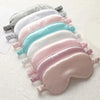 A set of ten silk sleep masks in various pastel colors, including pink, blue, and gray, laid out on a white surface.