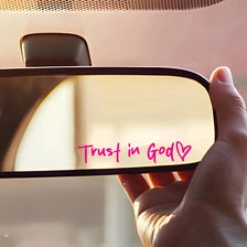 A hand holds a light-colored vinyl sticker with the text Trust in God and a heart symbol on it.