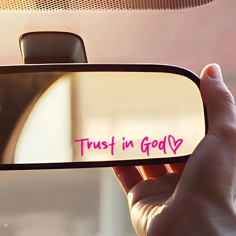 A hand holds a light-colored vinyl sticker with the text Trust in God and a heart symbol on it.