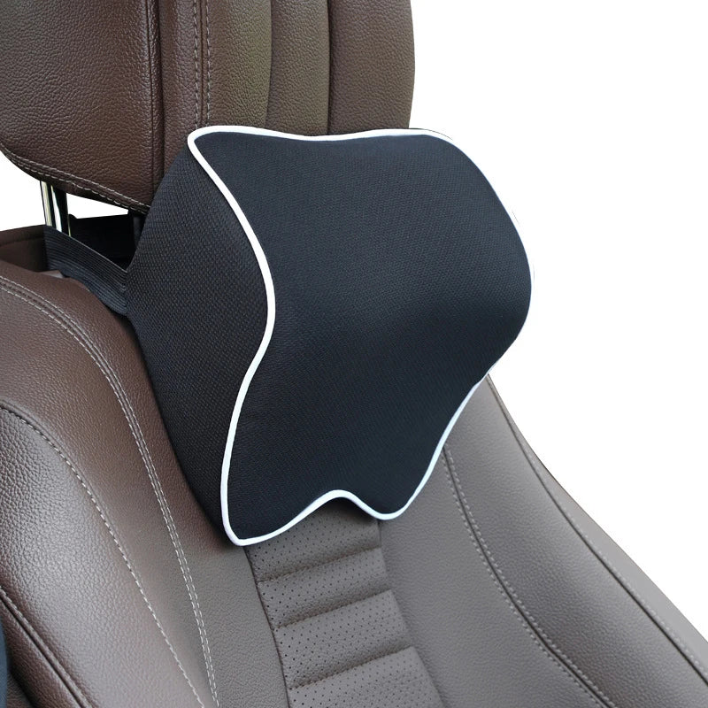 Black memory foam neck pillow with an adjustable strap placed on a brown car seat headrest.