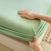 A hand is adjusting a light green fitted sheet on a mattress.