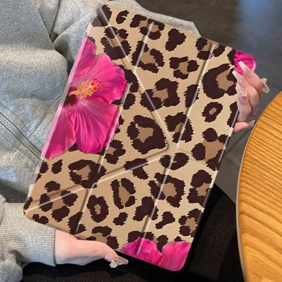 A leopard print floral tablet case for an iPad is held in a person's hand against a dark background.