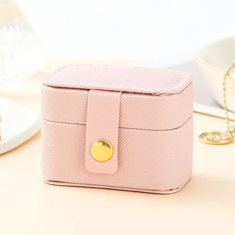 A pink compact leather jewelry travel case with a gold-colored clasp resting on a light surface.