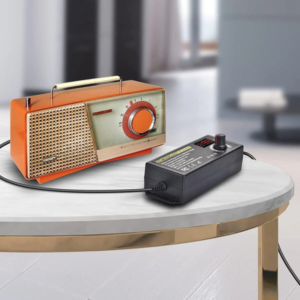 Orangefarbene und silberne, verstellbare AC-auf-DC-Netzteil-Adapter auf einem weißen Tisch.