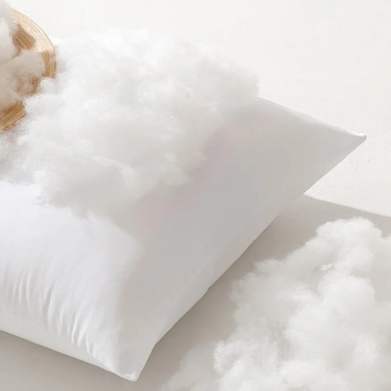 A white square cushion filled with fluffy white polyester fiber, resting on a light surface.