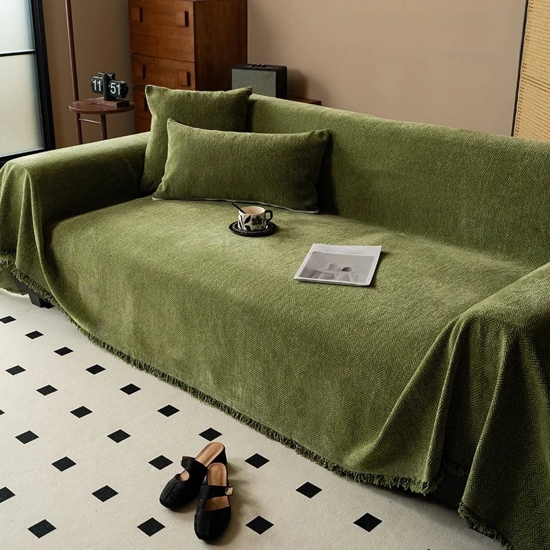 A moss green chenille sofa throw with tassel edges draped over a sofa on a light rug.