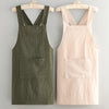 A pair of premium cotton kitchen aprons, one olive green and one pale pink, displayed on wooden hangers.