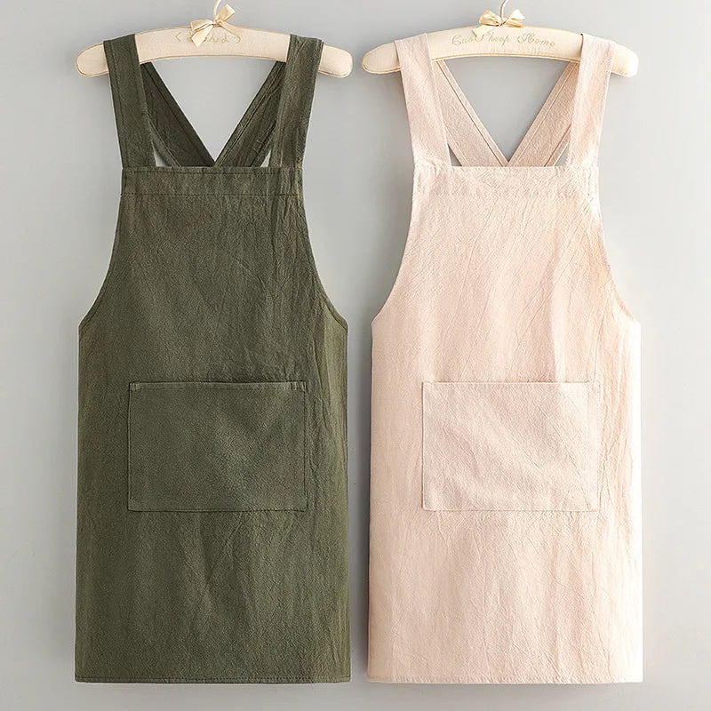A pair of premium cotton kitchen aprons, one olive green and one pale pink, displayed on wooden hangers.