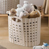 A white folding laundry basket filled with soft stuffed toys and a straw hat