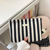 Un sac pochette en crochet rayé noir et blanc est exposé dans un tiroir blanc à côté d'un grand jouet en peluche.