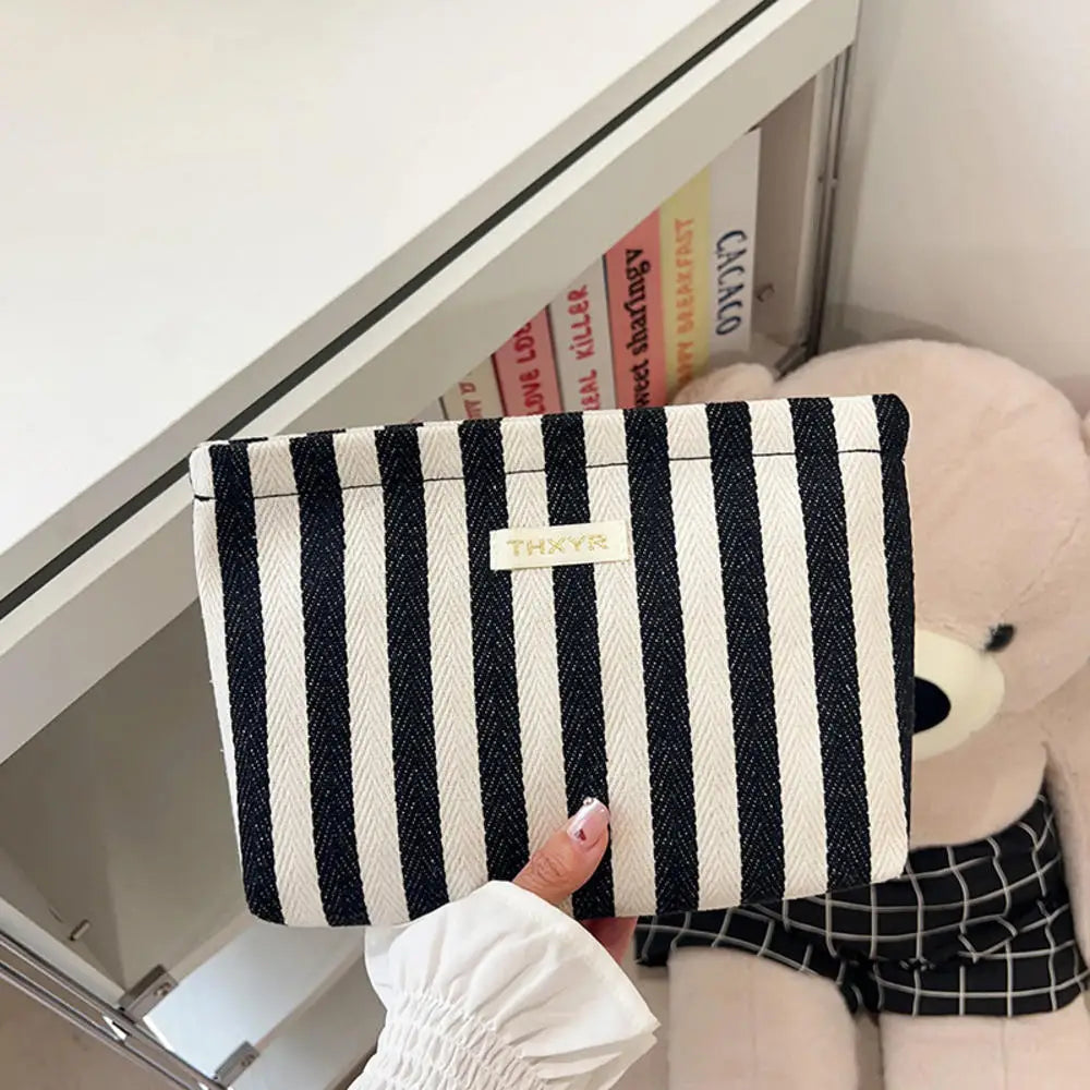 Un sac pochette en crochet rayé noir et blanc est exposé dans un tiroir blanc à côté d'un grand jouet en peluche.