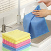 A hand is cleaning a surface with a blue cloth, surrounded by stacks of colorful reusable microfiber cleaning cloths.