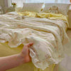 A hand is holding a light yellow floral washed cotton gauze summer quilt with delicate embroidery.