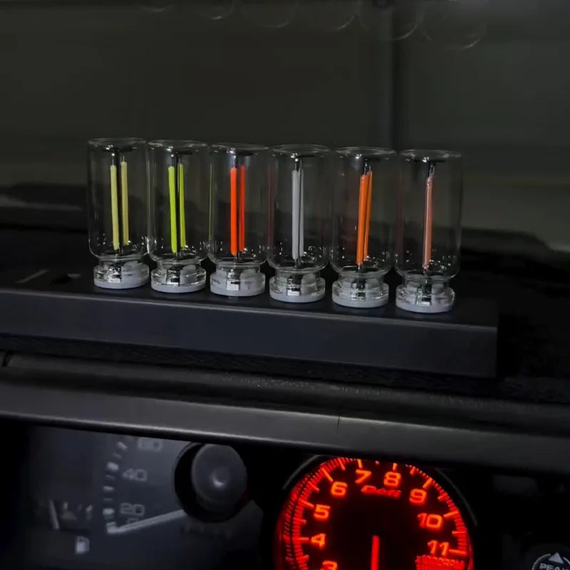 A row of glass tubes containing various colored LED filaments resting on a dark surface.