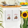 A set of two white kitchen towels featuring a festive Christmas design on red pickup trucks.