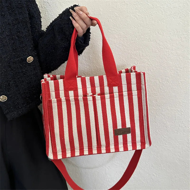 A person holds a red and white striped canvas tote bag with inner pockets against a light background.