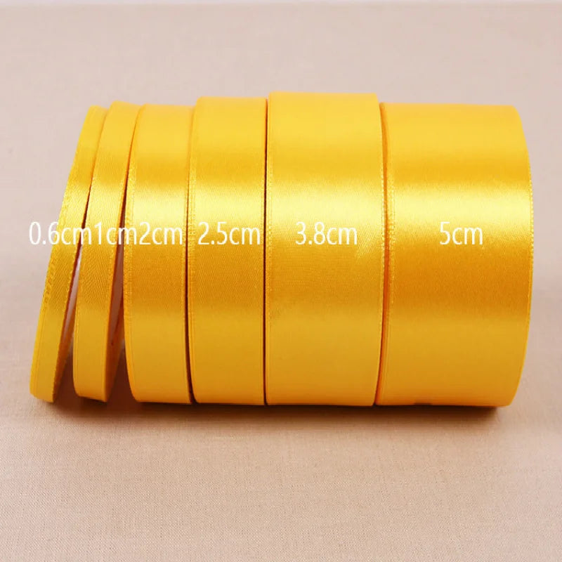 Eine Rolle goldgelber Seiden-Satin-Band mit verschiedenen Breiten nebeneinander