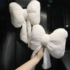 A white plush bowknot car headrest pillow with neck support is being held by a hand.