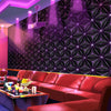 A modern interior featuring a dark geometric wallpaper, red leather seating, and purple accent lighting.