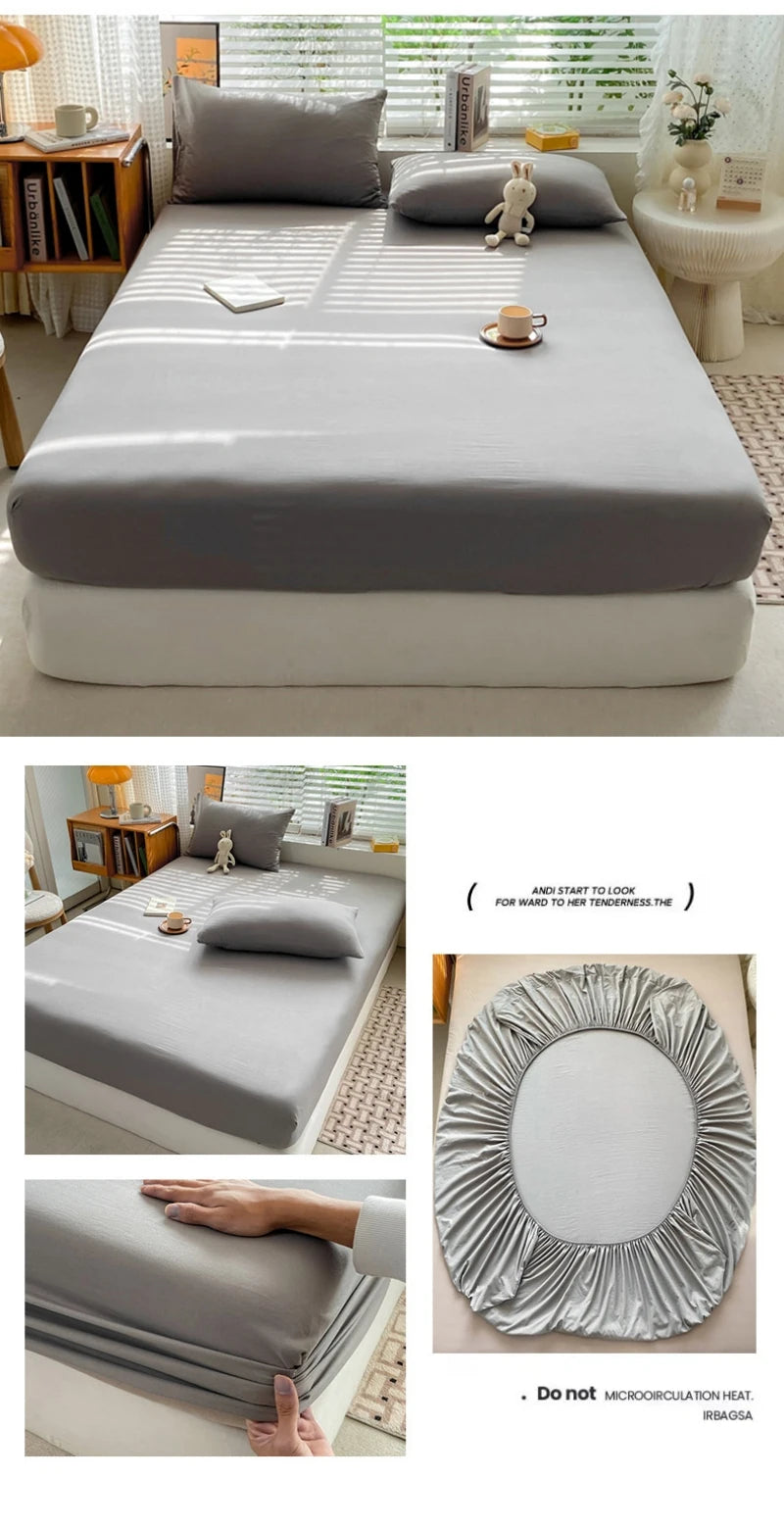 A fitted sheet in solid gray fabric is shown folded and laid out on a bed, with a hand demonstrating its elastic band.