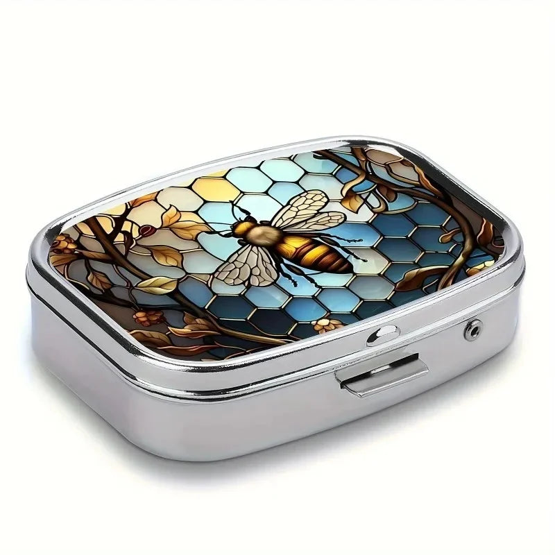 A silver metal pill organizer and jewelry case with a hexagonal, nature-themed inlay featuring a bee and foliage.