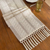 Beige bohemian farmhouse table runner with fringe detail on a wooden surface.
