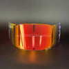 A replacement motorcycle helmet visor with a vibrant orange-red tint displayed on a dark surface.