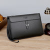 Schwarze Damen-Clutch aus Kunstleder mit silberner Hardware auf Holzoberfläche.