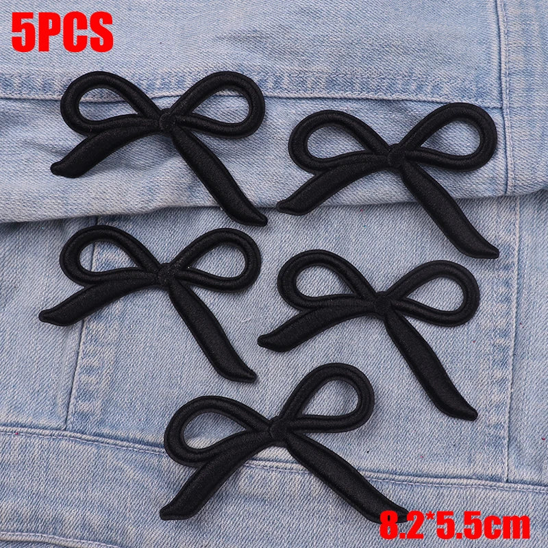 Five black embroidered bow iron-on patches displayed on a denim fabric background.