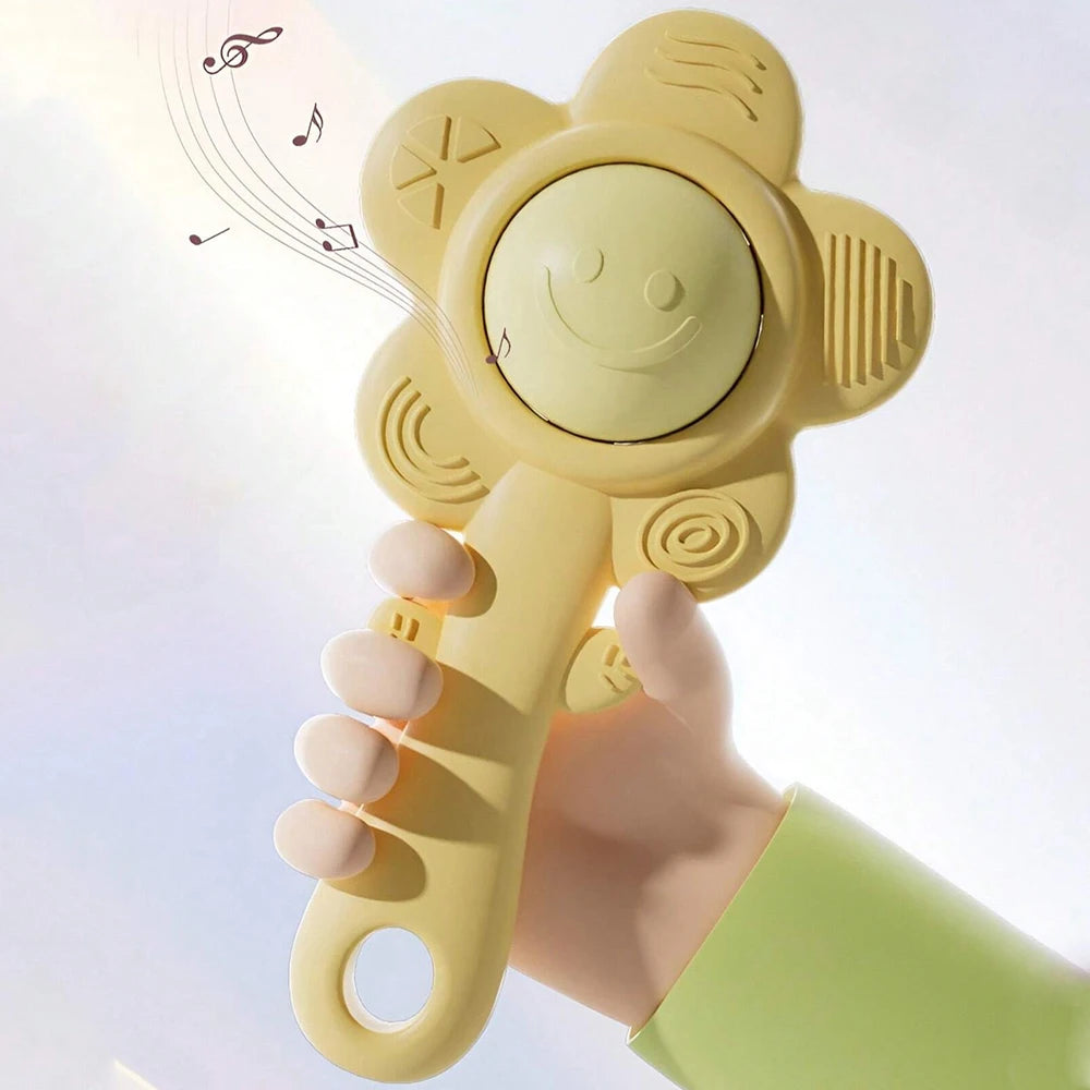 A hand holds a yellow silicone baby teething rattle toy with a smiley face and a grip for sensory play.
