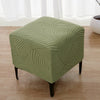 A square ottoman covered in a sage green geometric jacquard stretch fabric sitting on a wooden floor.