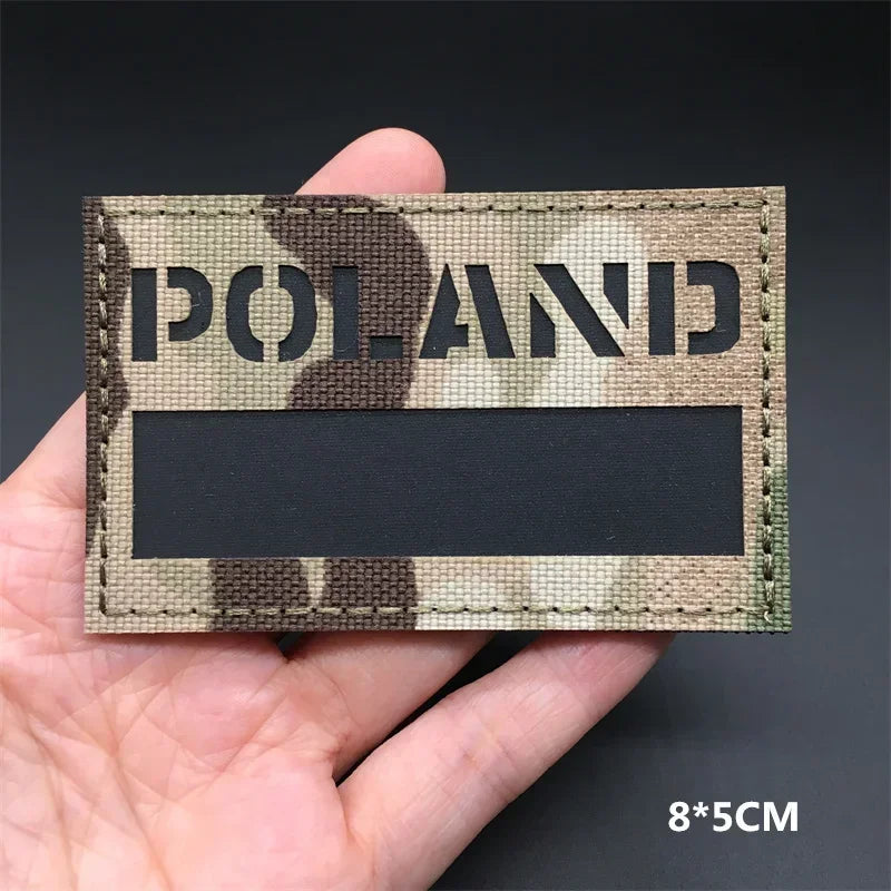 A rectangular tactical patch featuring a camouflage pattern with the word POLAND printed in dark lettering.