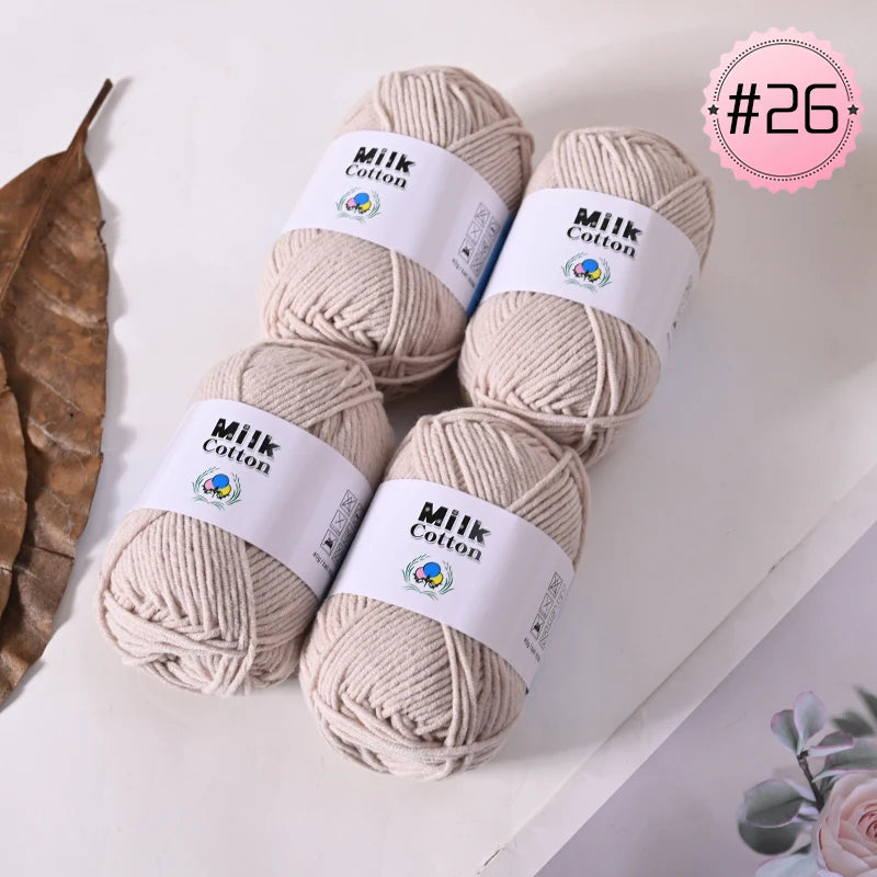 Four skeins of light beige milk cotton yarn are displayed on a white surface.